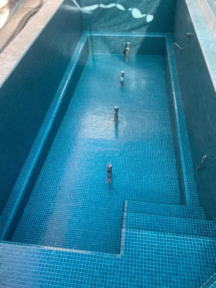 בריכה ריקה בחיפוי פסיפס כחול, עם מדרגות ומעברים בין הרצפה לדפנות